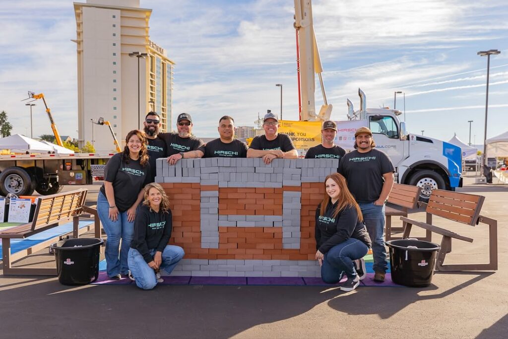 Hirschi Masonry poses together in front of their logo in Las Vegas, Nevada.